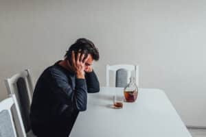 A man sitting with a glass and bottle of alcohol wondering how to wean off alcohol.