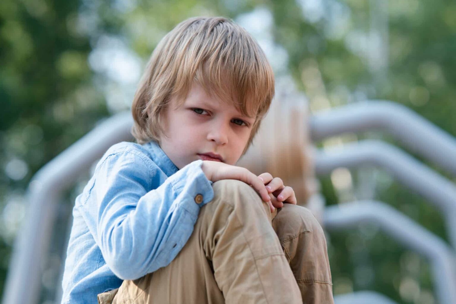 pensive child sitting with knees up outside